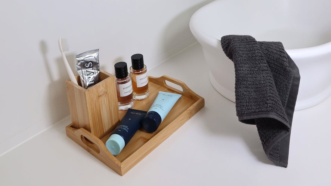 AKJ SKIN products displayed on a bathroom tray beside a basin, with a hand towel — minimal and modern skincare setup.