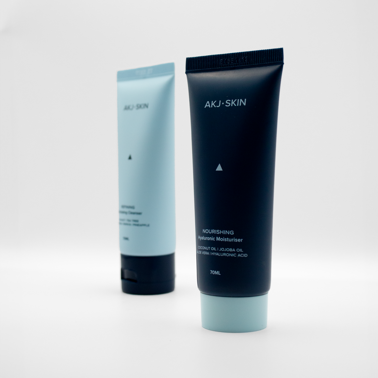Close-up of AKJ SKIN Nourishing Hyaluronic Moisturiser in focus, with AKJ SKIN Exfoliating Cleanser blurred in the background against a clean white backdrop.